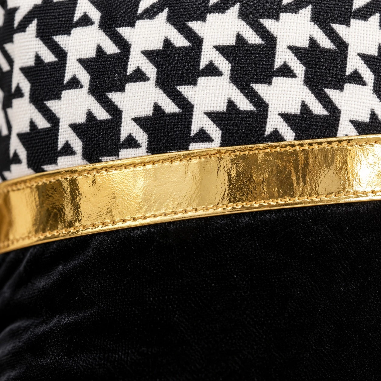 Close-up of black and white houndstooth fabric, a gold metallic band and black velvet on the cushion cover